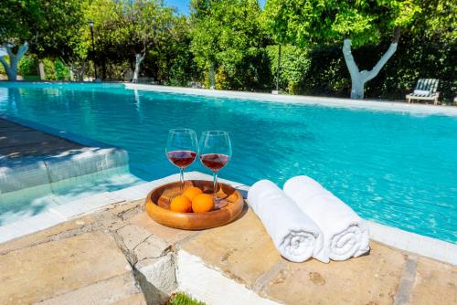 a bowl of fruit and two glasses of wine next to a swimming pool at Huerta la Pimentada in Palma del Río