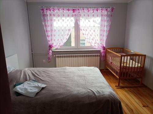 a bedroom with a crib and a window with pink curtains at Noclegi w Dolinie Drwęcy in Kurzętnik