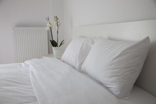 ein weißes Bett mit weißer Bettwäsche und einer Vase aus Blumen in der Unterkunft CASA Di TRE in Thessaloniki