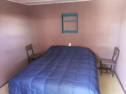 1 dormitorio con 1 cama azul y 2 sillas en Viajes & Vida km0 en San Pedro de Atacama