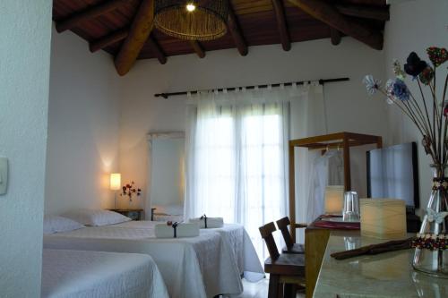 a bedroom with two beds and a table and a window at Vila dos Caetés - Suíte 03 - Barra do Sahy in Barra do Sahy