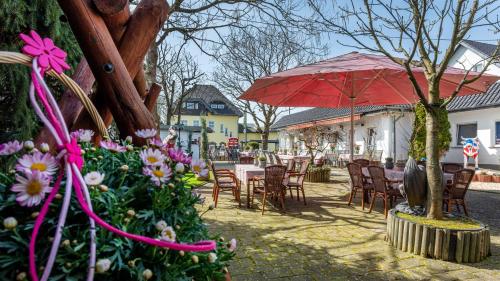 un patio con mesas, sillas y una sombrilla roja en The Little Britain Inn Themed Hotel One of a Kind In Europe en Vettelschoß