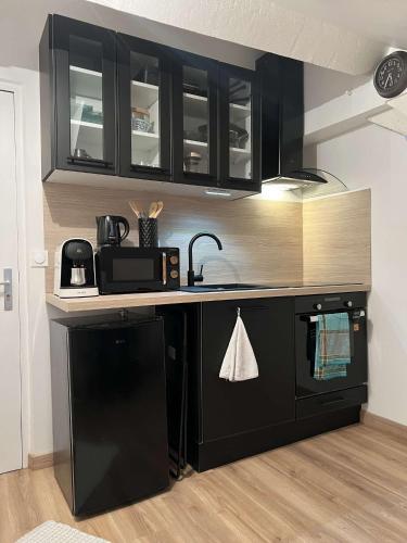 une cuisine avec des armoires noires et un appareil noir dans l'établissement Le Concon Versaillais, à 5 minutes du Château de Versailles, à Le Chesnay