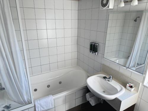 a white tiled bathroom with a sink and a tub at Arena Lodge in Palmerston North