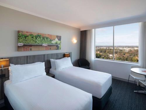 a hotel room with two beds and a window at Mercure Sydney Bankstown in Bankstown