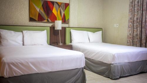 two beds in a hotel room with white sheets at Suites del Sol Hotel & Apartments in Mérida