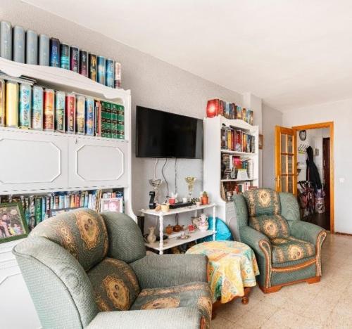 sala de estar con 2 sillas, TV y libros en Habitaciones privadas con cama doble en Sevilla, en Sevilla