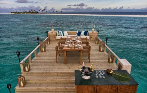 a wooden dock with a table and chairs on the water at Finolhu, A Seaside Collection Resort, a Member of Design Hotels in Baa Atoll