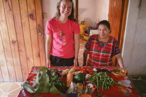 dos mujeres de pie junto a una mesa de verduras en POSADA DOÑA ELENA LA COMADRONA en San Juan La Laguna