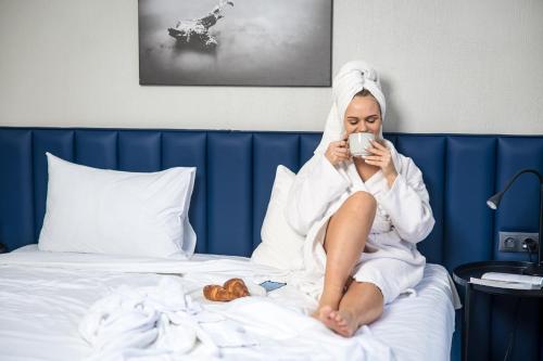 Kobieta siedząca na łóżku pijąca kawę w obiekcie Žilvinas Hotel w Połądze