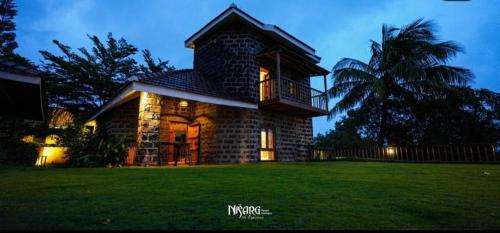 a small brick house with a balcony on a lawn at Nisarg Resort in Kolhapur