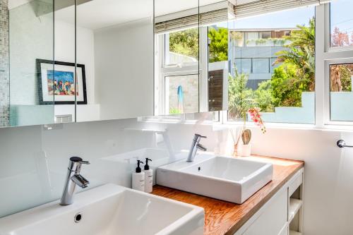 a white bathroom with two sinks and windows at Beach Steps in Cape Town