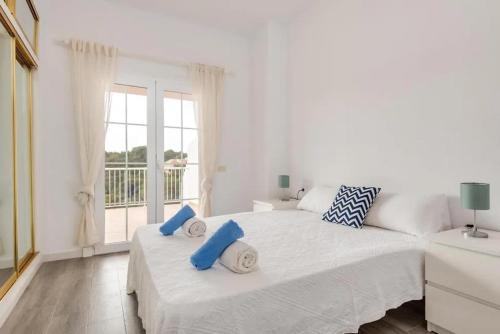 a white bedroom with a large bed with blue pillows on it at Ca n'Ernest in Cala Galdana