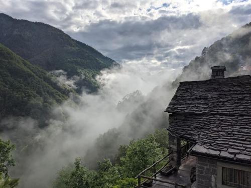 a view of a misty mountain with a house in the foreground at Wild Valley Puro Ticino 1+2 in Valle Onsernone in Crana