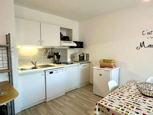 une petite cuisine avec des armoires blanches et une table dans l'établissement Appartement proximité mer, à Saint-Gilles-Croix-de-Vie
