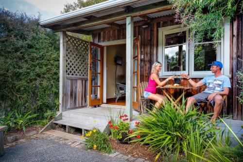 a man and woman sitting at a table outside of a tiny house at The Church Accommodation in Hahei