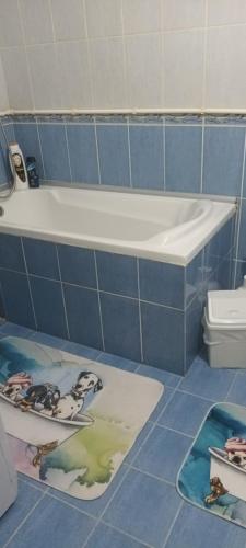 a blue tiled bathroom with a bath tub and mats on the floor at Apartman Gaga in Pirot