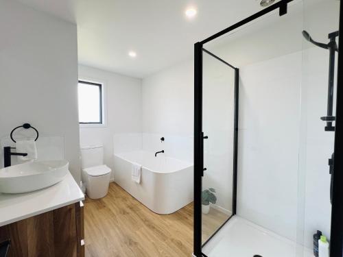 a white bathroom with a tub and a sink at Leisure Holiday Home Lake Hayes Easte Queenstown in Arrowtown