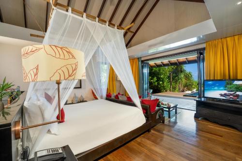 a bed with a net in a room with a tv at Atmosphere Kanifushi - Premium All Inclusive with Free Transfers in Lhaviyani Atoll