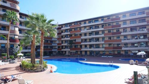 a large apartment building with a swimming pool and palm trees at Türkiz Kánaán Apartman in Puerto de Santiago