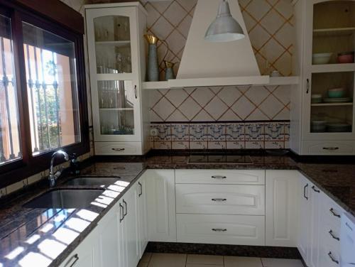cocina con armarios blancos, fregadero y ventana en Villa Martiniano, en Campano