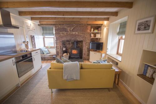 a living room with a yellow couch and a stone fireplace at The Wee House in Pennan