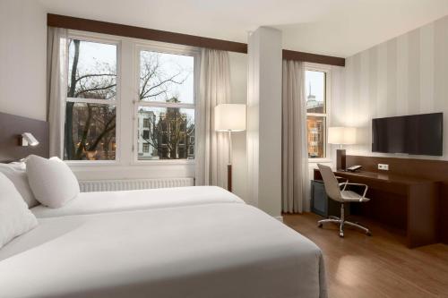a hotel room with a bed and a desk and window at NH City Centre Amsterdam in Amsterdam