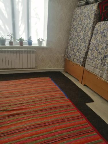 ein Wohnzimmer mit einem Teppich, einem Fenster und einem Bett in der Unterkunft Гостевой дом (Hostel) in Kochkorka