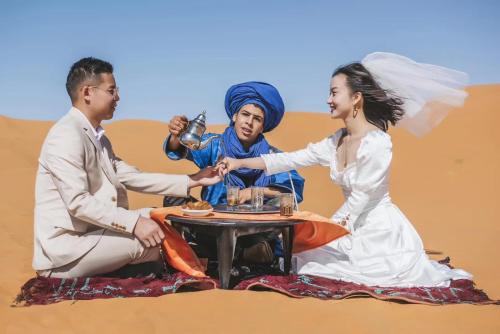 Una novia y un novio sentados alrededor de una mesa en el desierto en Sahara Dream luxury Camp, en Merzouga