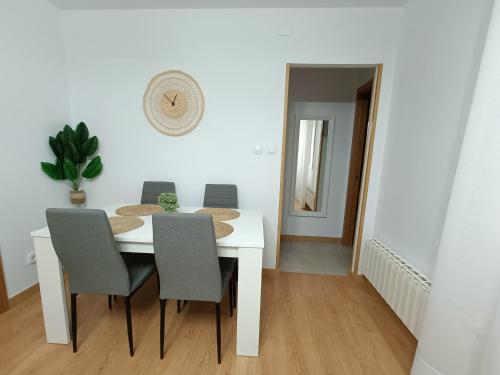 uma mesa de jantar branca com cadeiras e um relógio na parede em Apartamento La Planchada em El Astillero