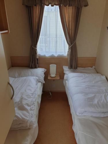 two beds in a room with a window at 3 bed static caravan in Chapel Saint Leonards