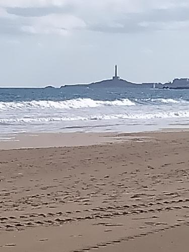 a person walking on a beach with a lighthouse in the ocean at Hotel Apartamentos Londres La Manga in La Manga del Mar Menor