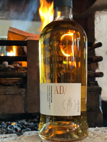 a bottle of alcohol sitting on a table in front of a fire at Roam West in Fort William