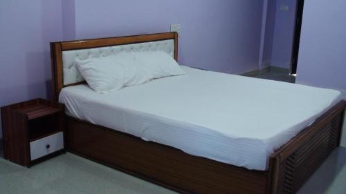 1 cama grande con marco de madera y sábanas blancas en HOTEL GOLDEN BUDDHA INN, en Bodh Gaya