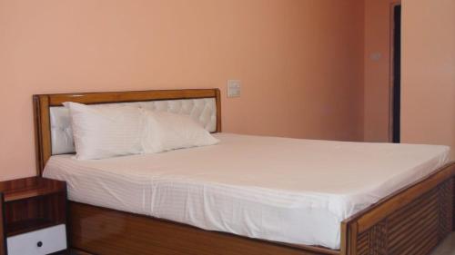 1 cama con marco de madera y sábanas y almohadas blancas en HOTEL GOLDEN BUDDHA INN, en Bodh Gaya