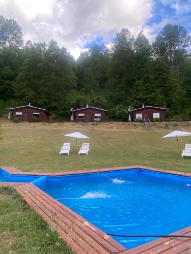a swimming pool with two lawn chairs and umbrellas at Cabañas de Montaña Deumayen in Caburgua