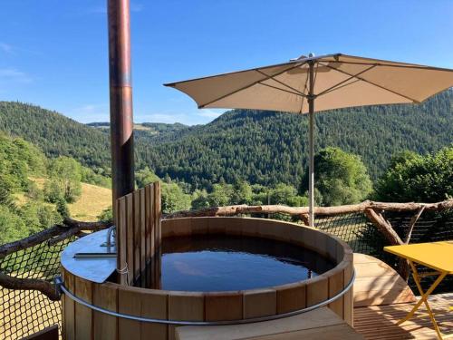 a hot tub with an umbrella on a deck at Cabane des Vargottes : insolite en pleine nature in Girmont-Val-dʼAjol