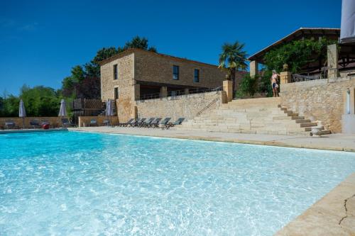 une piscine avec de l'eau bleue devant un immeuble dans l'établissement Hôtel La Villa Romaine, à Carsac-Aillac