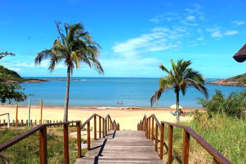 a wooden pathway leading to a beach with palm trees at Encanto Guarapari in Guarapari