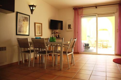 une salle à manger avec une table, des chaises et une télévision dans l'établissement Village naturiste - Jardin de la Palmeraie - Villa 2 chambres -, au Cap d'Agde