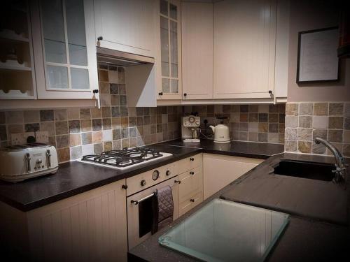 a kitchen with white cabinets and a stove top oven at Woodys Retreat Cosy One Bed Cottage in Belper
