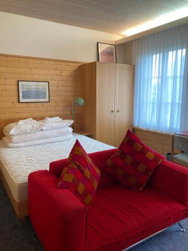 1 dormitorio con 1 cama y 1 sofá rojo en FriendsHouse Appenzellerhof, en Speicher