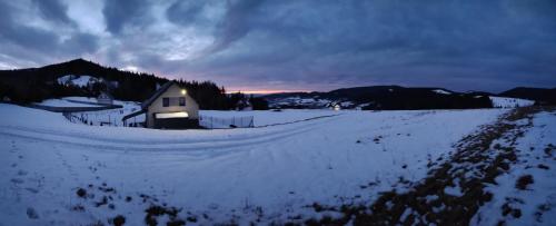 ein Haus auf einem schneebedeckten Feld mit Sonnenuntergang im Hintergrund in der Unterkunft BliżejGorców in Lubomierz