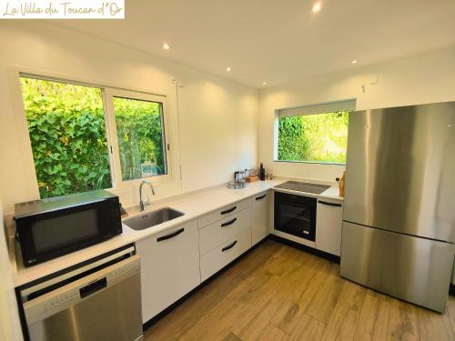 a kitchen with white cabinets and a sink and a refrigerator at La Villa du Toucan d'Or, au cœur de la Guadeloupe in Petit-Bourg
