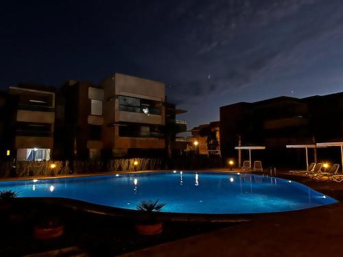 ein großer blauer Pool in der Nacht mit Gebäuden in der Unterkunft Appartement Golf City Prestigia Marrakech in Marrakesch