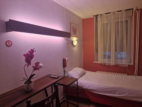 a room with a bed and a desk and a table with flowers at Hotel de l'Academie in Nancy