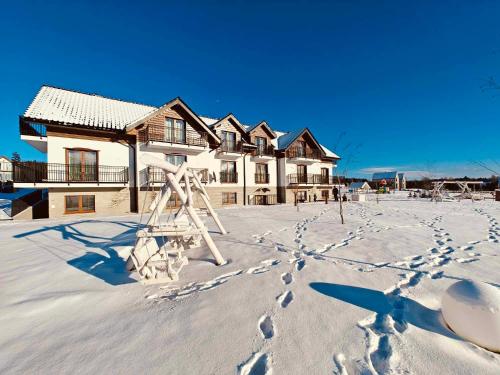 a snow covered yard with a house and a playground at Jagodowy Ski & Spa in Lasowka