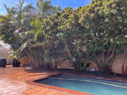 a swimming pool in a yard with palm trees at Lovely Garden Studio 2 - 10 minute walk to beach in Cape Town