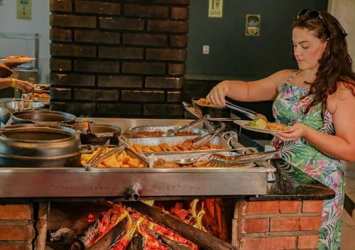 a woman holding a plate of food over a grill at Vale Encantado - Eco Park & Hotel in Biritiba-Mirim