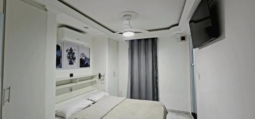 a white bedroom with a bed and a television at Apart Hotel Farol de Itapuã - Suíte com cozinha compacta à 250m da praia e farol de Itapuã in Salvador